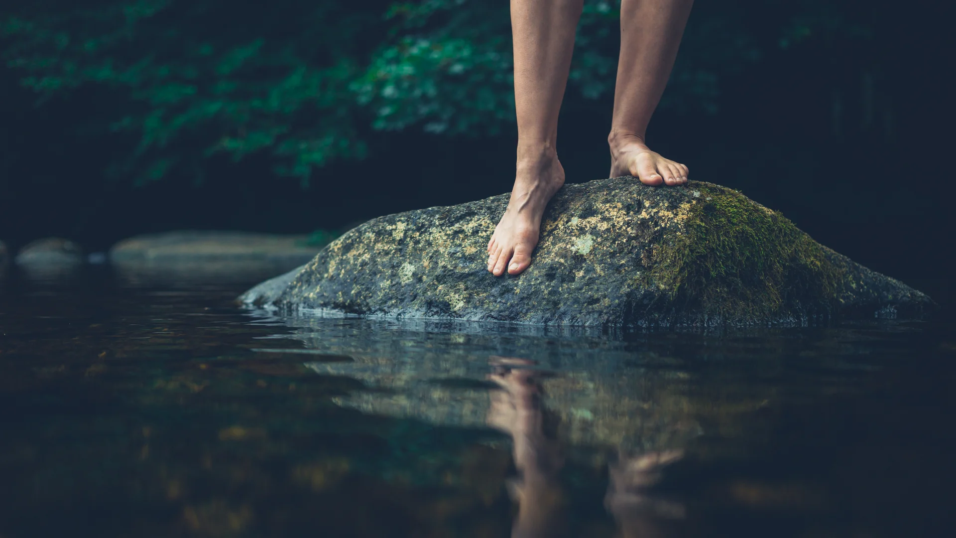 Barfuße Beine auf einem mit Moos bewachsenen Felsen über Wasser