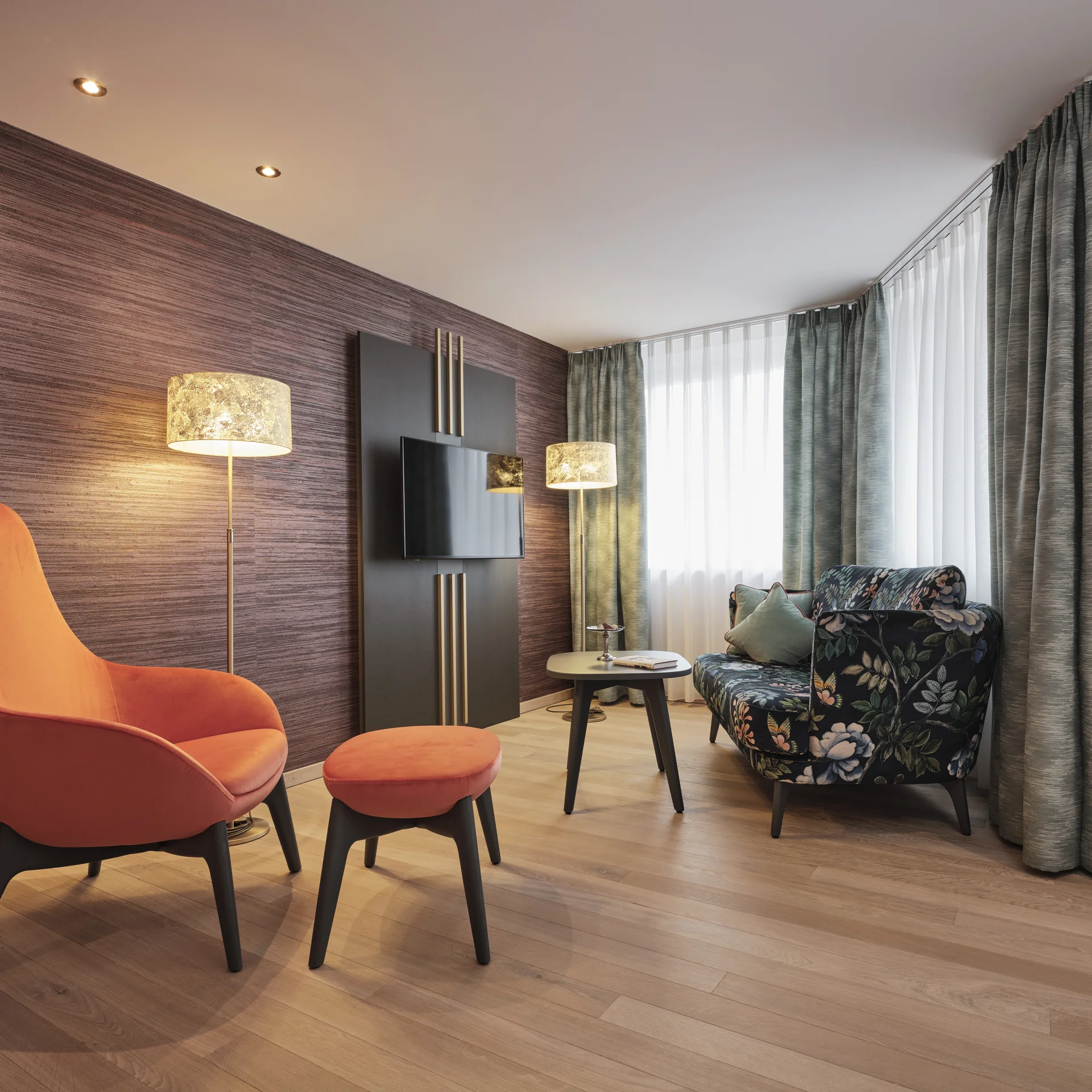 Modernes Wohnzimmer mit orangenem Sessel, Blumenmuster-Sofa und Stehlampen