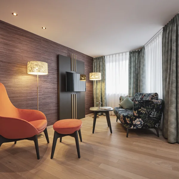 Modernes Wohnzimmer mit orangenem Sessel, Blumenmuster-Sofa und Stehlampen