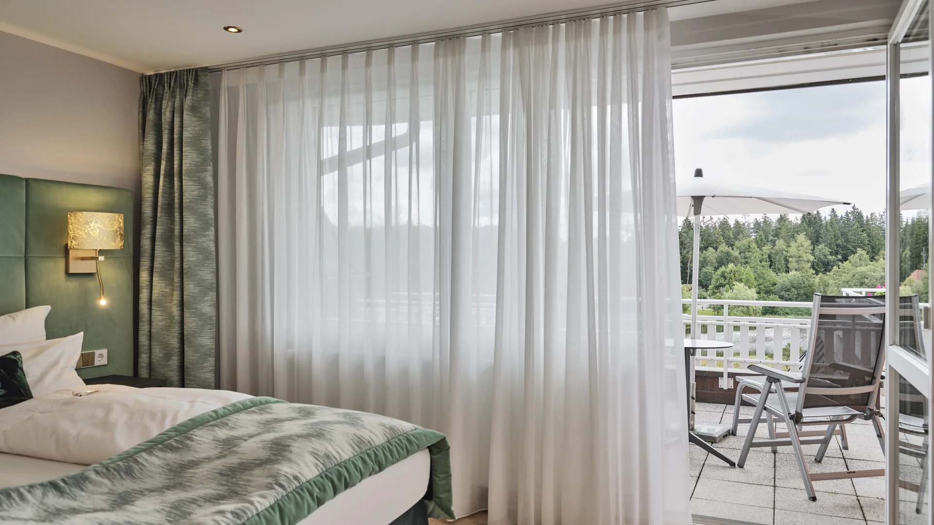 Moderner Hotelzimmerbereich mit Glas-Schiebetür und Balkon mit Tischen und Stühlen