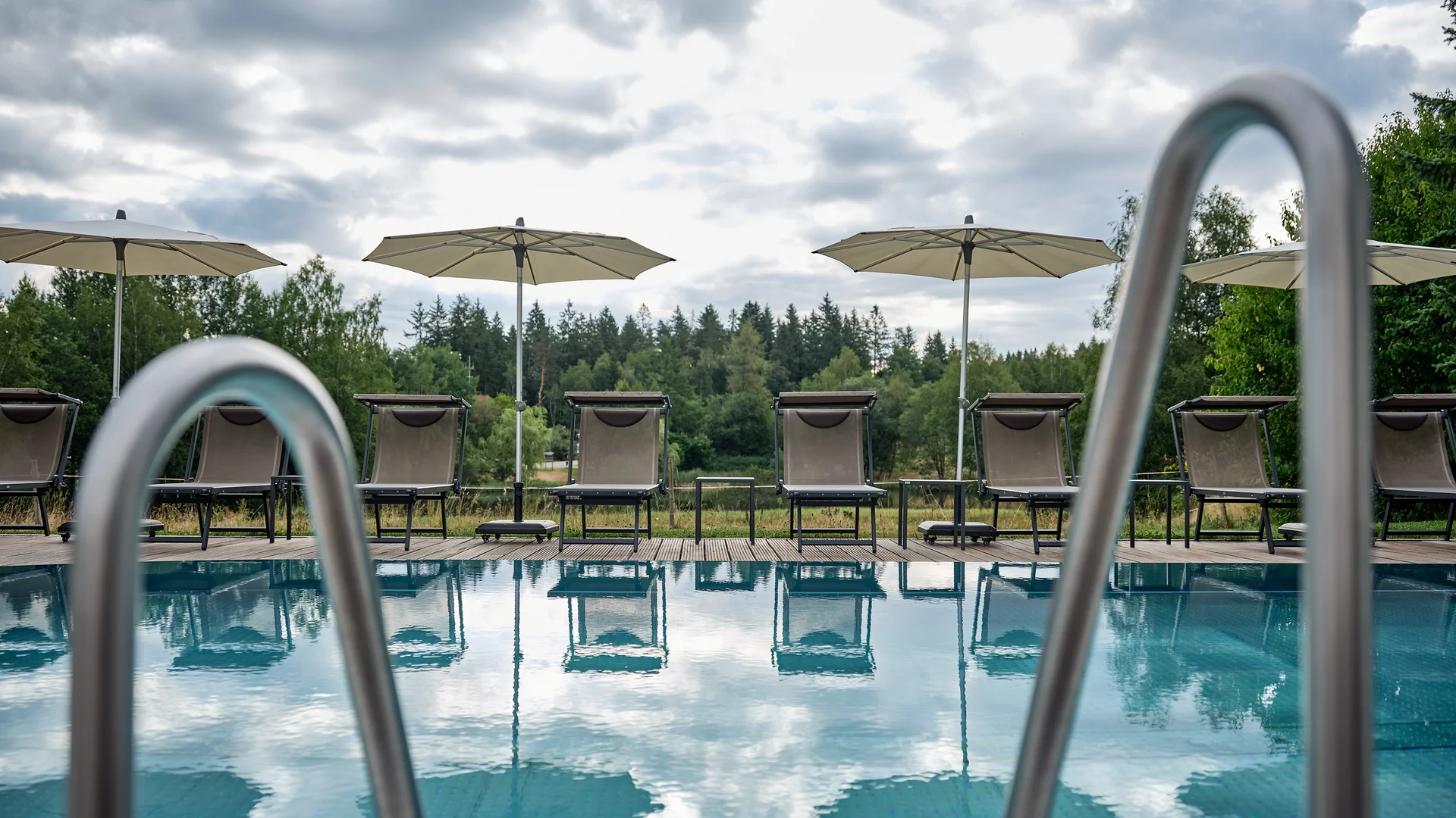 Blick auf leeren Pool mit Liegestühlen und Sonnenschirmen bei bewölktem Himmel