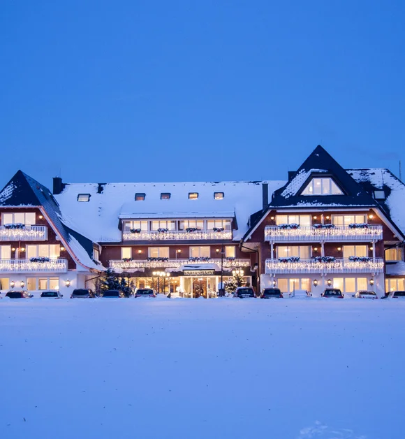 Beleuchtetes Hotel im Chaletstil in einer verschneiten Winterlandschaft bei Dämmerung