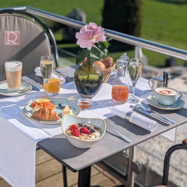 Table avec petit déjeuner et fleur rose sur terrasse avec vue verte