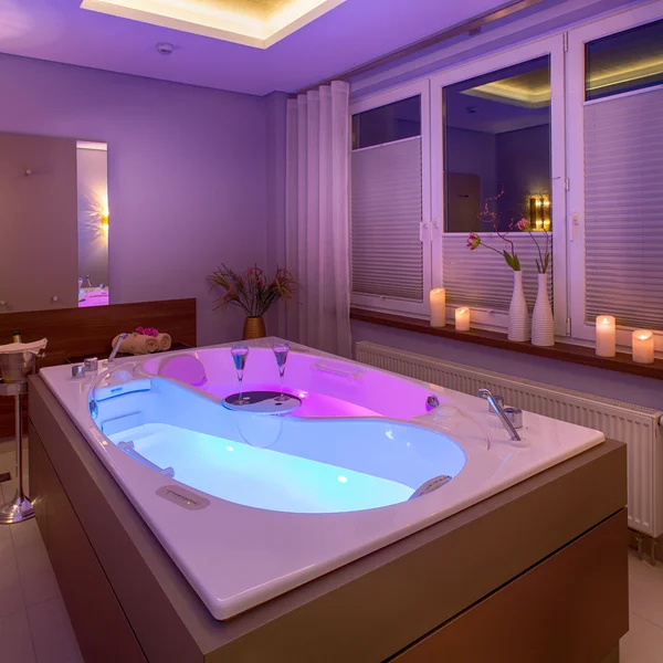Wellness-Badewanne mit beleuchtetem Wasser, Kerzen und Dekoration in einem modernen Raum