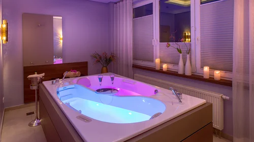 Wellness-Badewanne mit beleuchtetem Wasser, Kerzen und Dekoration in einem modernen Raum
