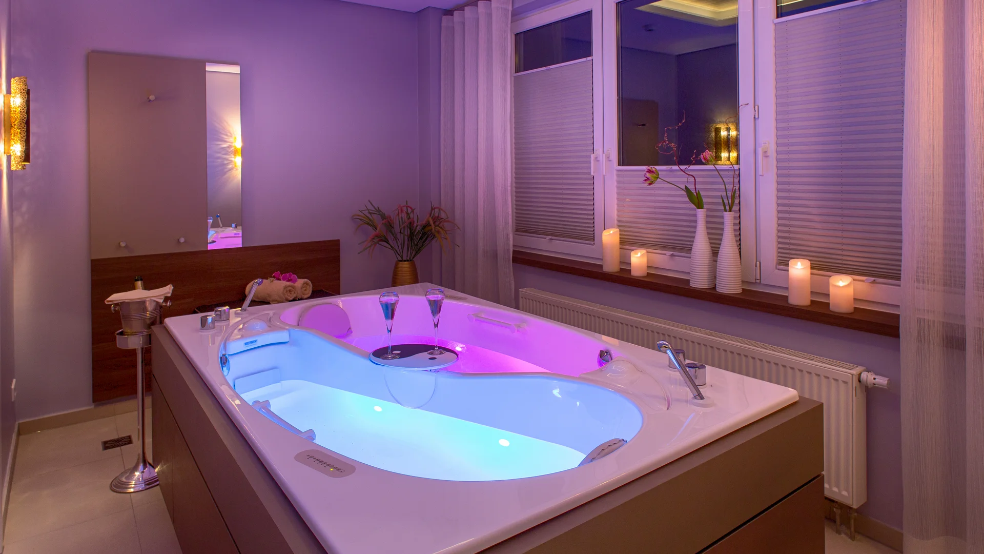 Wellness-Badewanne mit beleuchtetem Wasser, Kerzen und Dekoration in einem modernen Raum