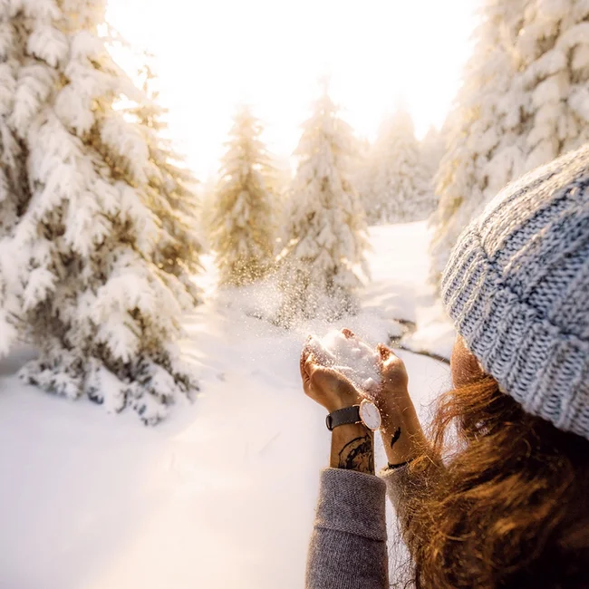 Frau wirft Schnee in einem sonnigen, verschneiten Tannenwald in die Luft