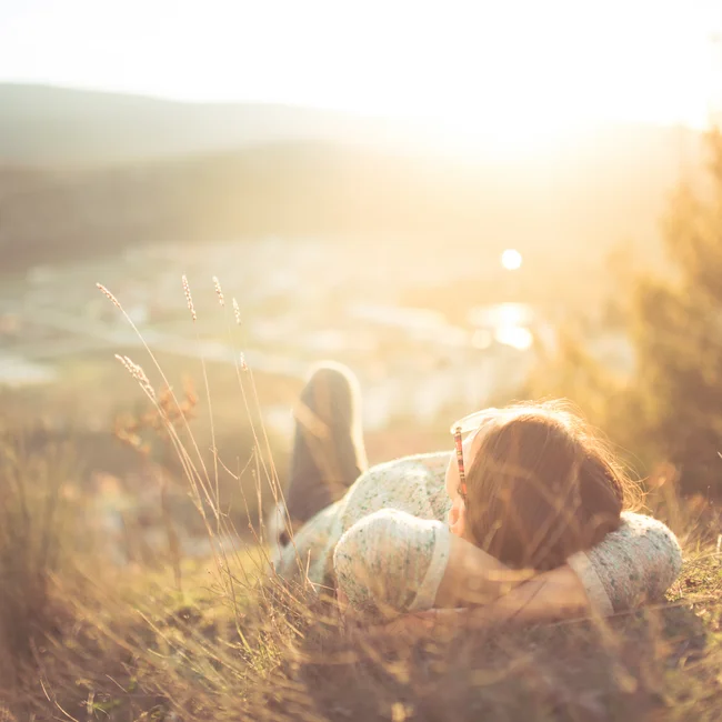 Person allongée dans l'herbe avec soleil et collines en arrière-plan