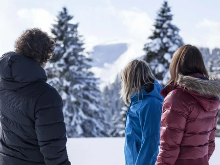 Trois personnes en vestes d’hiver admirent un paysage de montagne enneigé