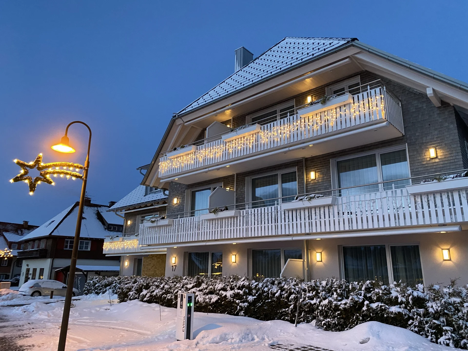 Bâtiment enneigé aux balcons illuminés et lampadaire décoré de lumières festives