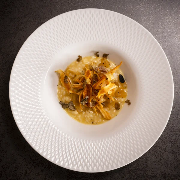 Köstliches Risotto mit Karottenchips und Trüffel auf weißem Teller