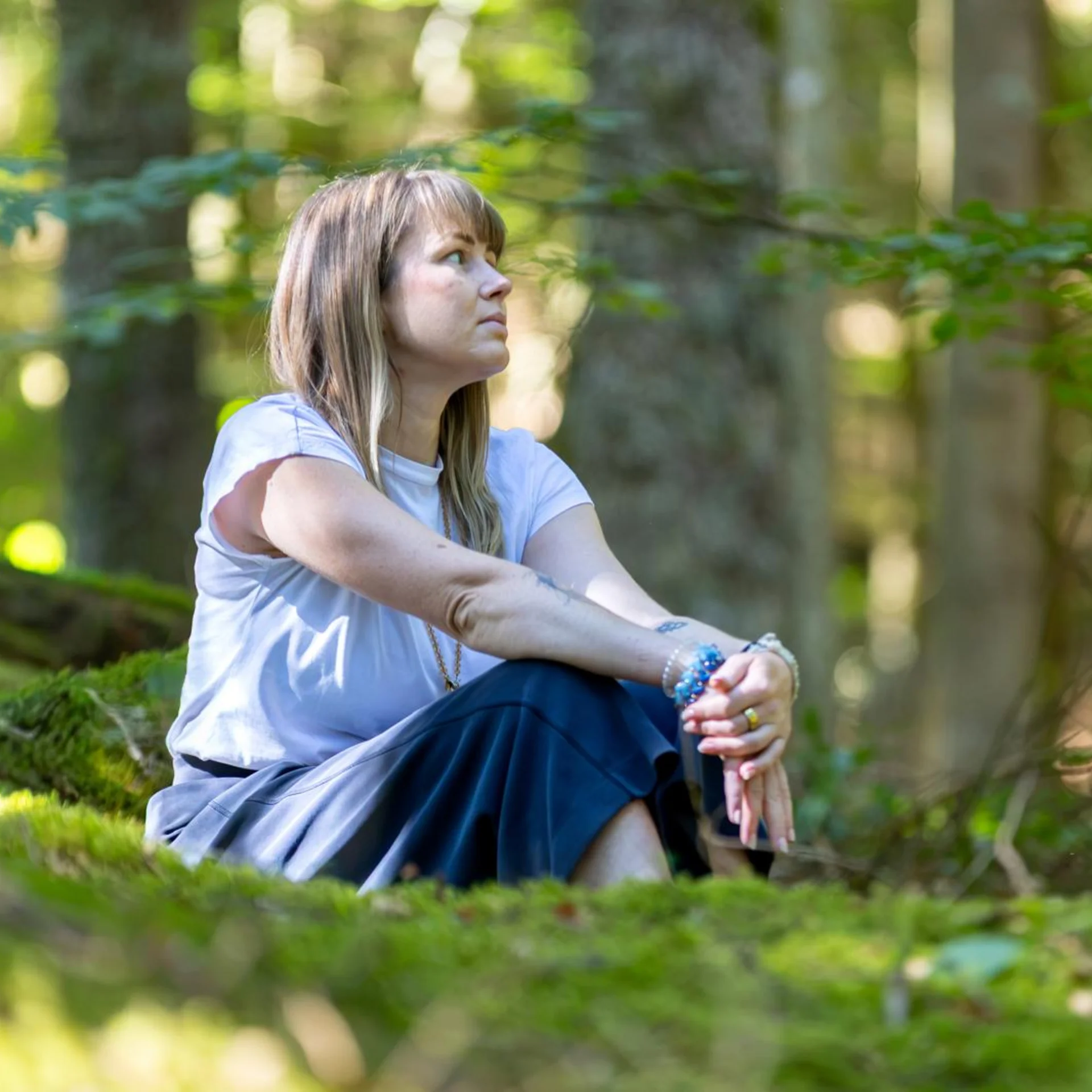 One Body, One Soul | Slow Living Hotel Reppert in Hinterzarten Frau sitzt nachdenklich auf moosigem Waldboden in sonnigem Wald