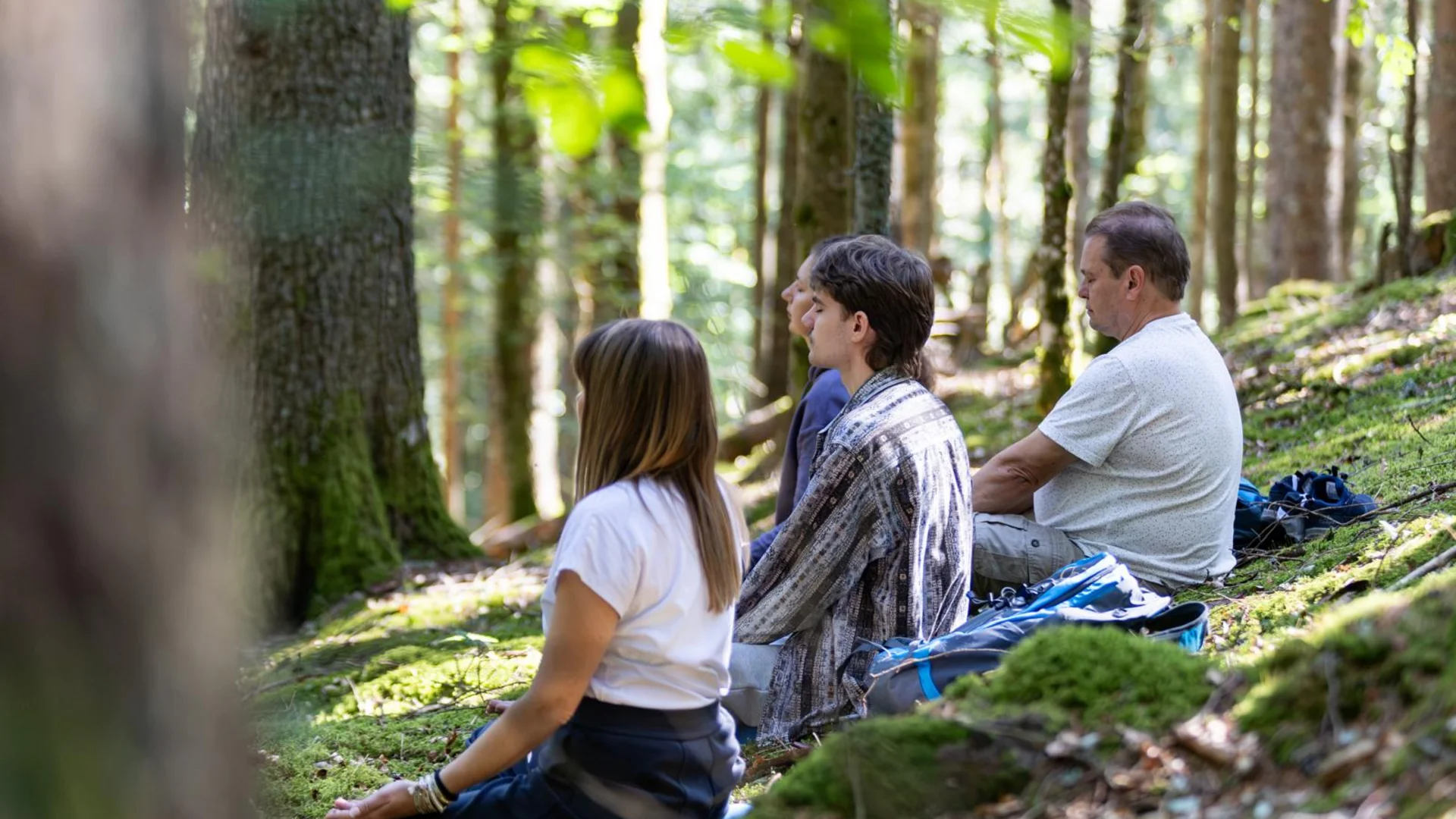 Hausprogramm | Slow Living Hotel Reppert in Hinterzarten Vier Personen sitzen entspannt im Wald auf moosbedecktem Boden