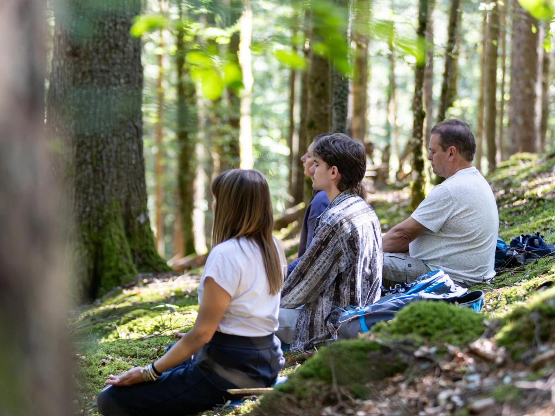 Yoga im Hotel im Schwarzwald | Reppert in Hinterzarten Vier Personen sitzen entspannt im Wald auf moosbedecktem Boden