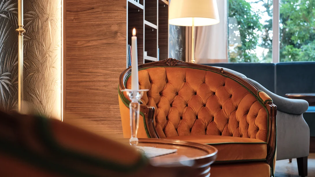 Inklusivleistungen | Slow Living Hotel Reppert Gemütlicher orangefarbener Sessel vor einem Fenster mit Lampe und Kerze
