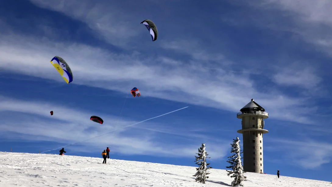 Des ailes de snowkite au-dessus d’une colline enneigée, avec une tour et des arbres givrés