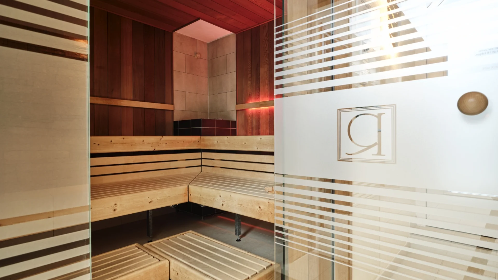 Sauna mit hölzernen Sitzbänken und Glas-Eingangstür