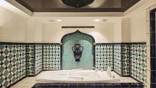 Badewanne mit blau-grünen Fliesen und dekorativer Vase an der Wand