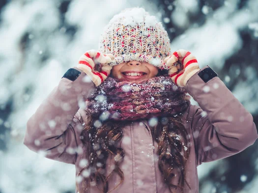 Kind mit Schneemütze und Handschuhen spielt lachend im Schnee