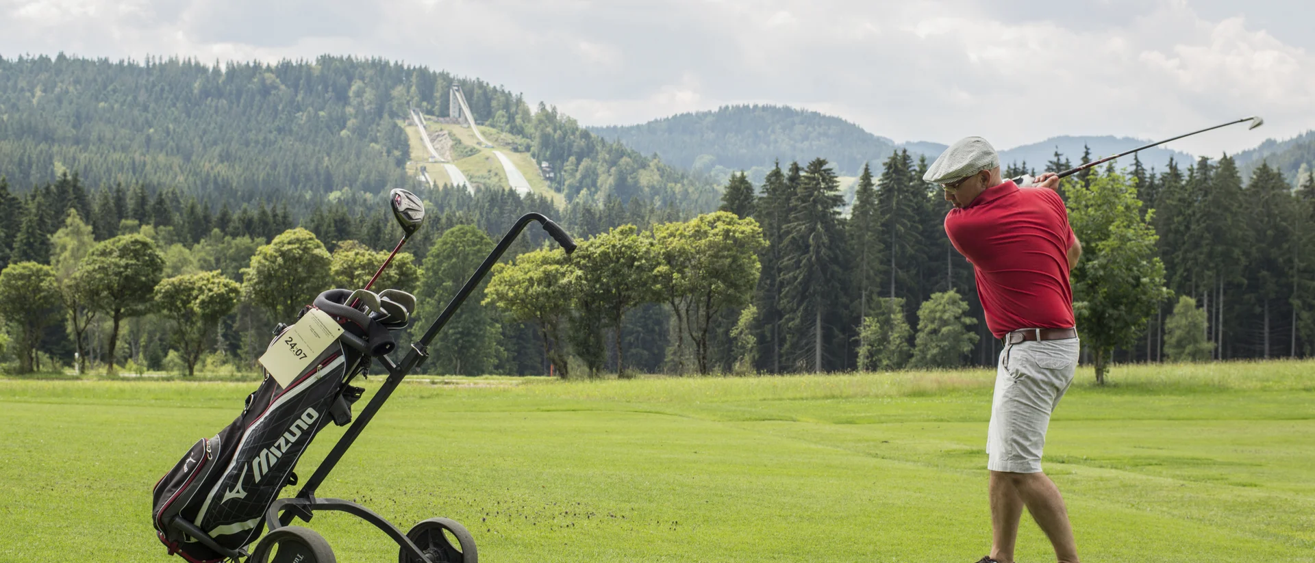 Golfer schlägt Ball auf grünem Golfplatz mit Bergen im Hintergrund