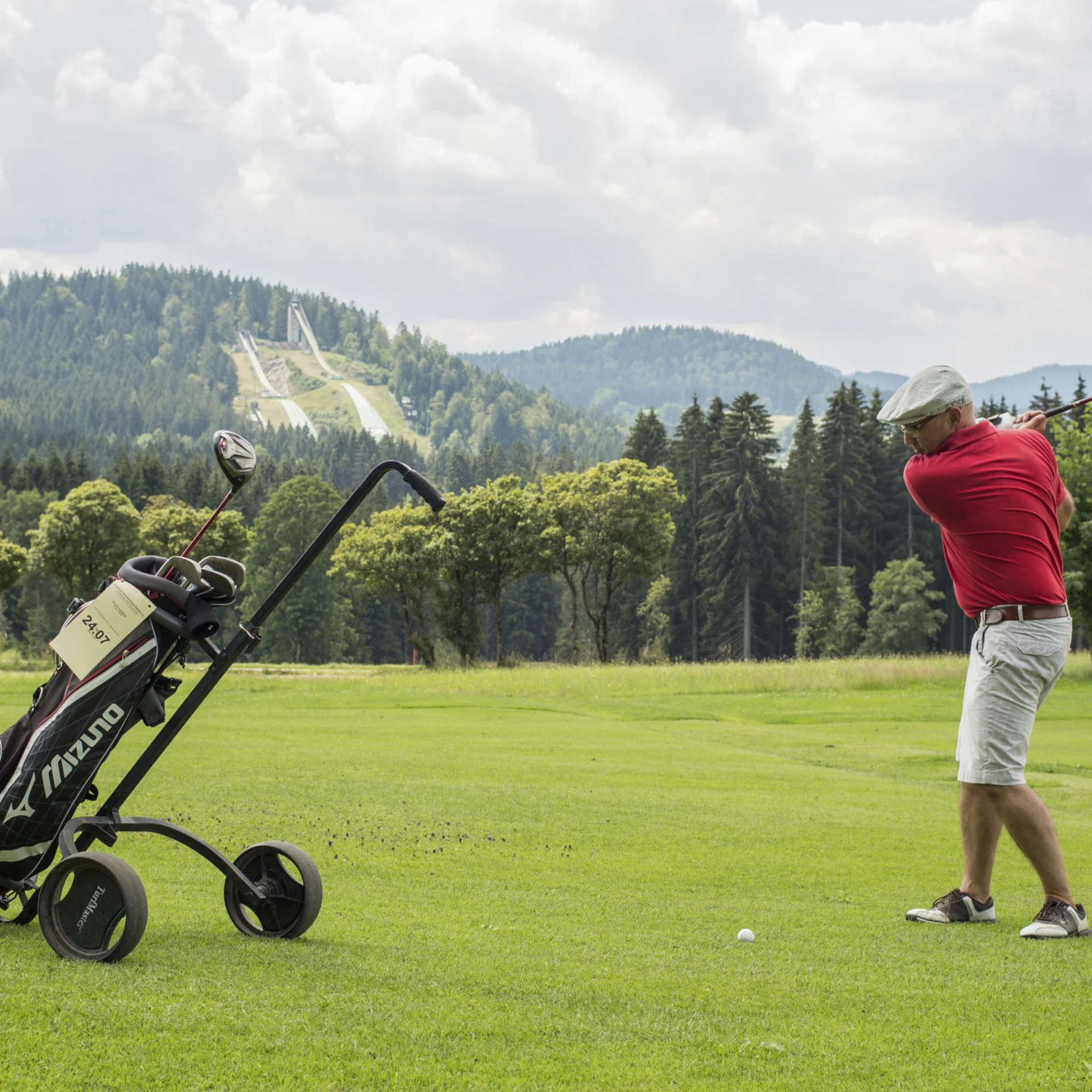Golfer schlägt Ball auf grünem Golfplatz mit Bergen im Hintergrund