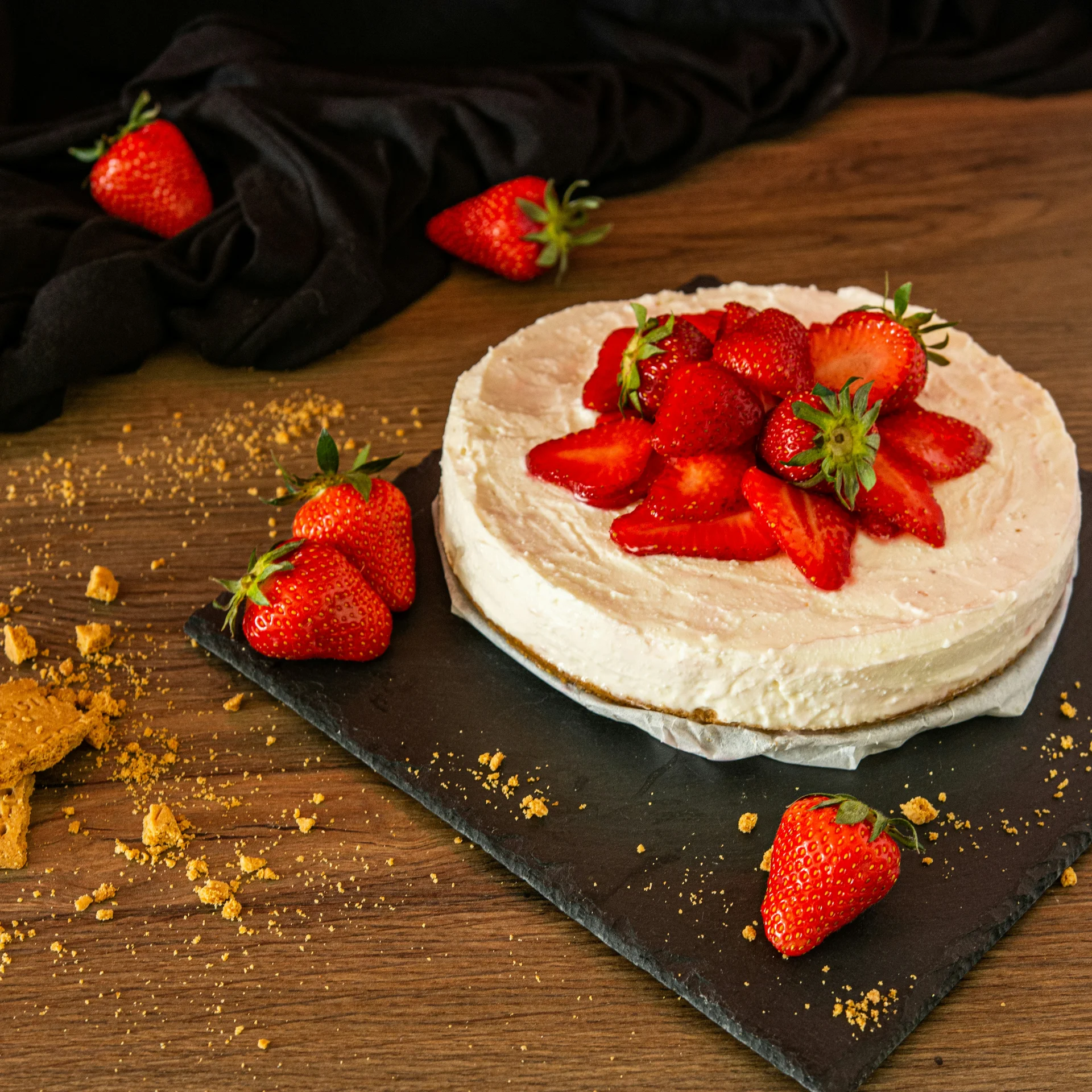 Erdbeerkuchen auf schwarzem Brett mit verstreuten Kekskrümeln