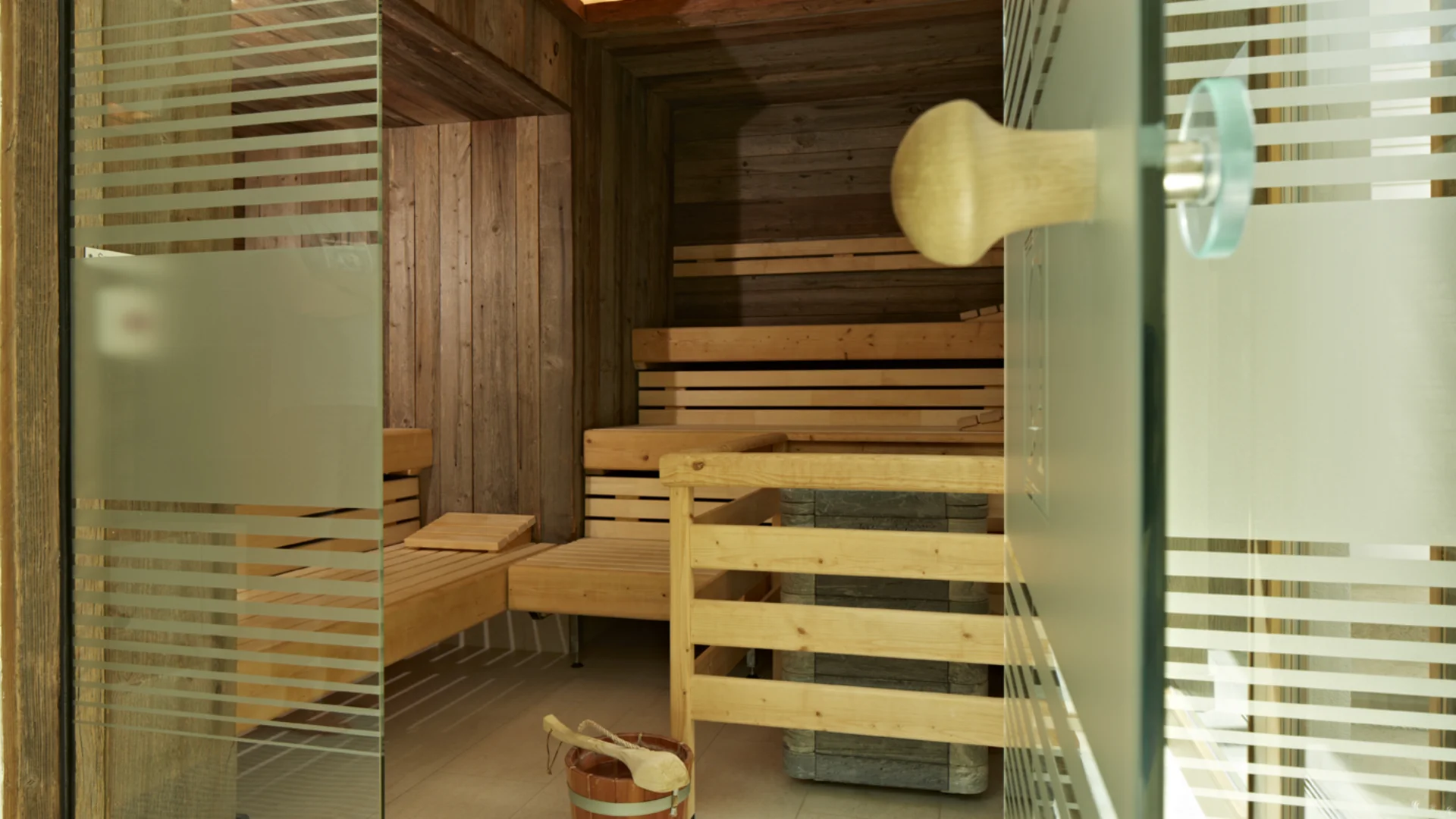 Innenansicht einer Sauna mit Holzbänken und einem Eimer mit Schöpflöffel