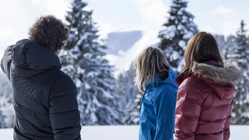 Drei Personen blicken auf schneebedeckte Bäume und Berge im Winter
