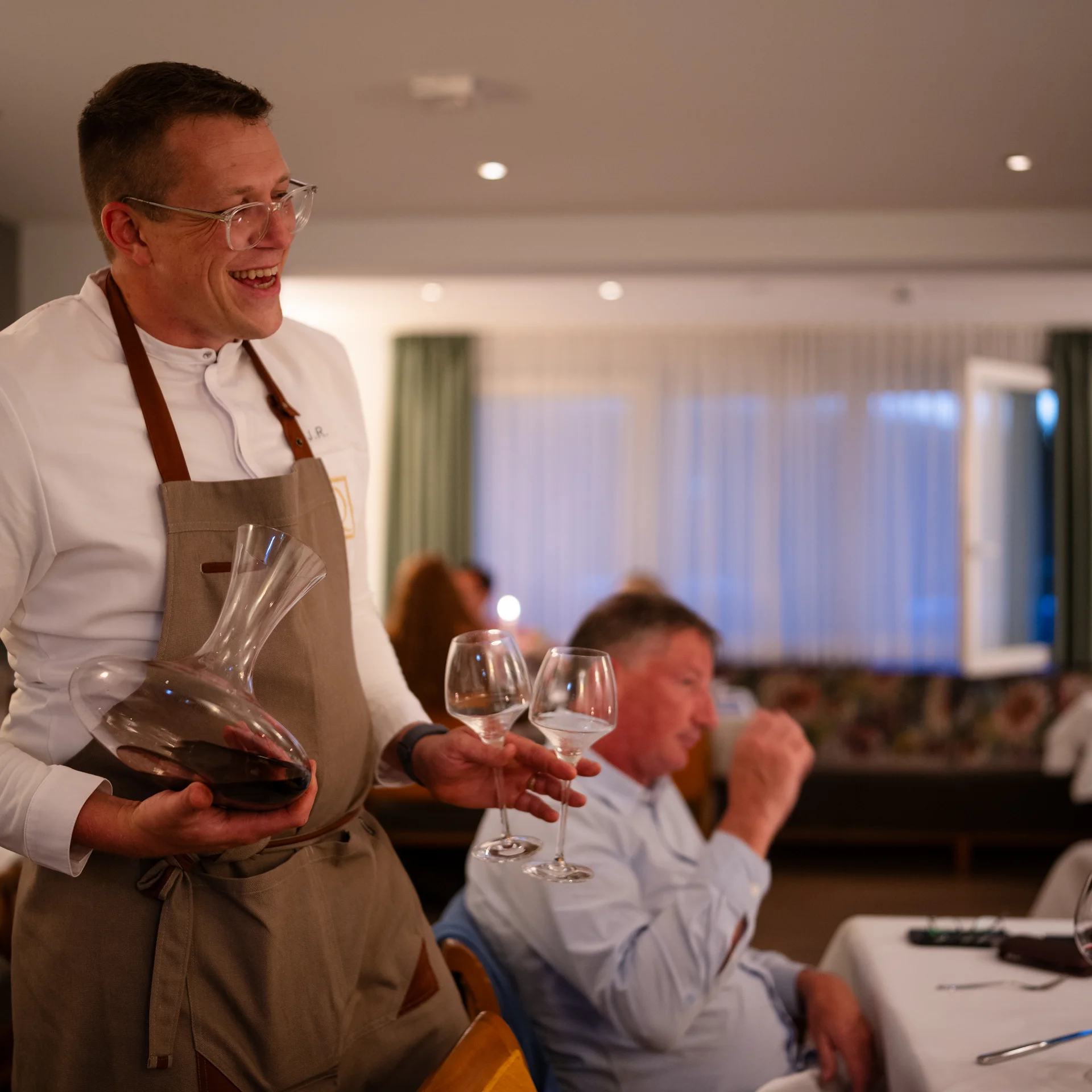 Kellner mit Karaffe und Weingläsern in einem belebten Restaurant