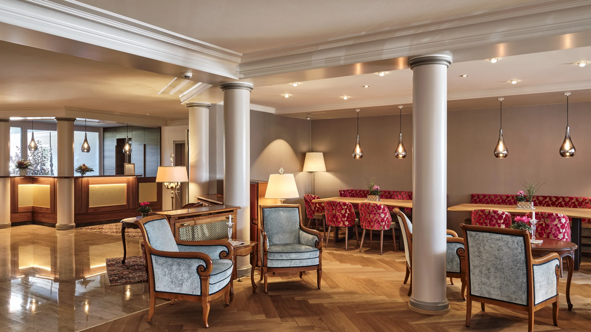 Heller Hotel-Lobbybereich mit Säulen, Sesseln und roten gepolsterten Stühlen