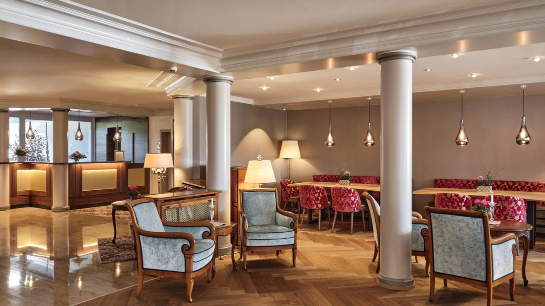 Heller Hotel-Lobbybereich mit Säulen, Sesseln und roten gepolsterten Stühlen