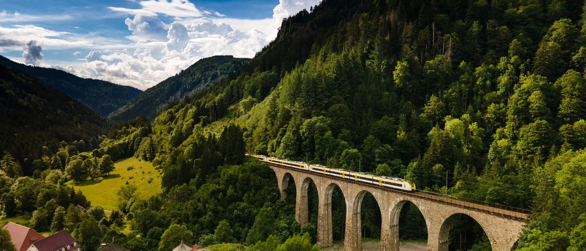 Wandern rund um Hinterzarten im Schwarzwald Zug fährt über einen Steinbogenviadukt in bewaldeten Bergen bei klarem Himmel