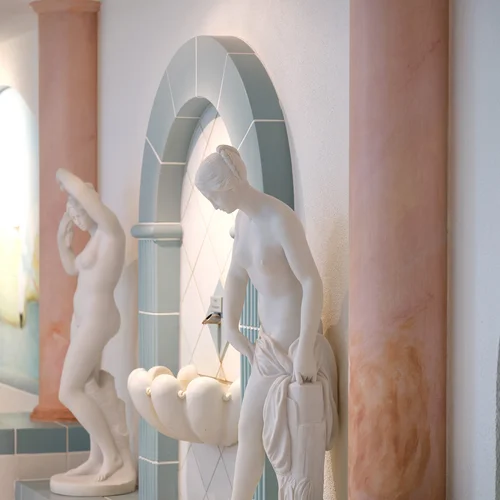 Statues blanches devant des arches et colonnes dans un intérieur clair