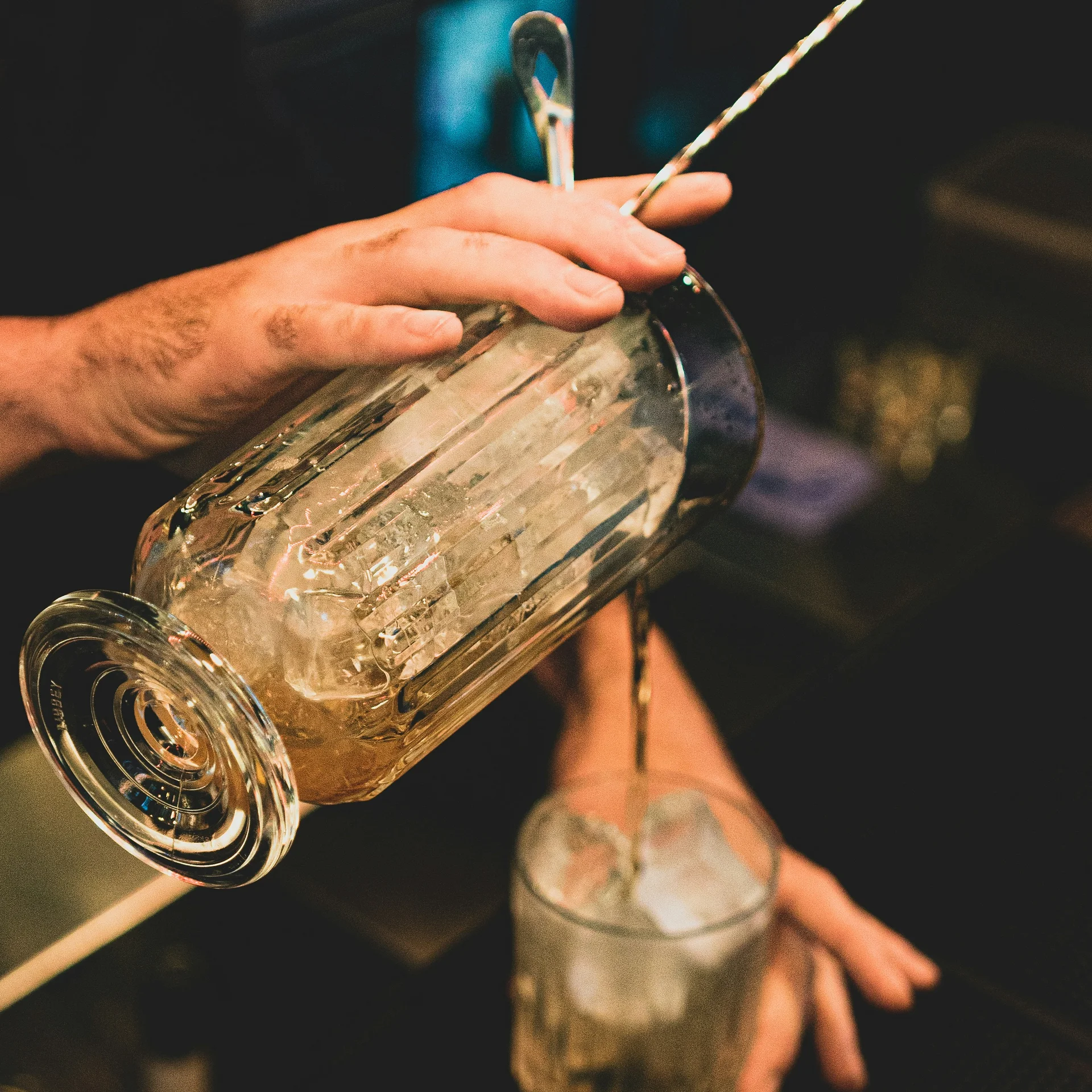 Hand gießt ein Getränk mit Eiswürfeln aus einem Shaker ins Glas