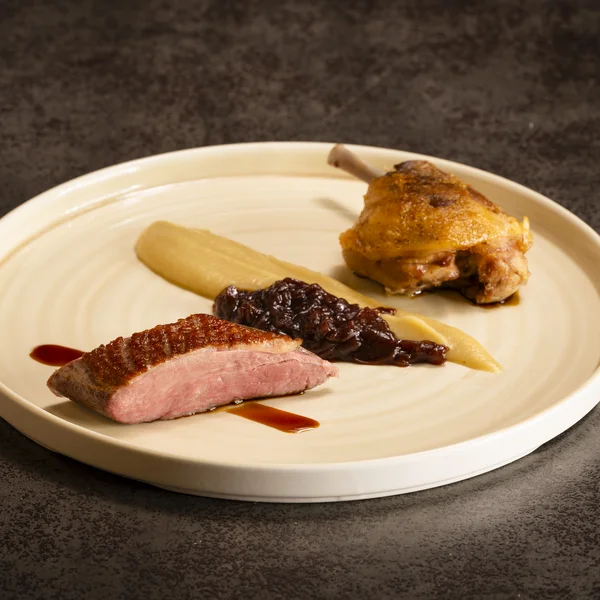 Gourmet-Gericht mit Entenbrust, Entenkeule und Sauce auf cremefarbigem Teller