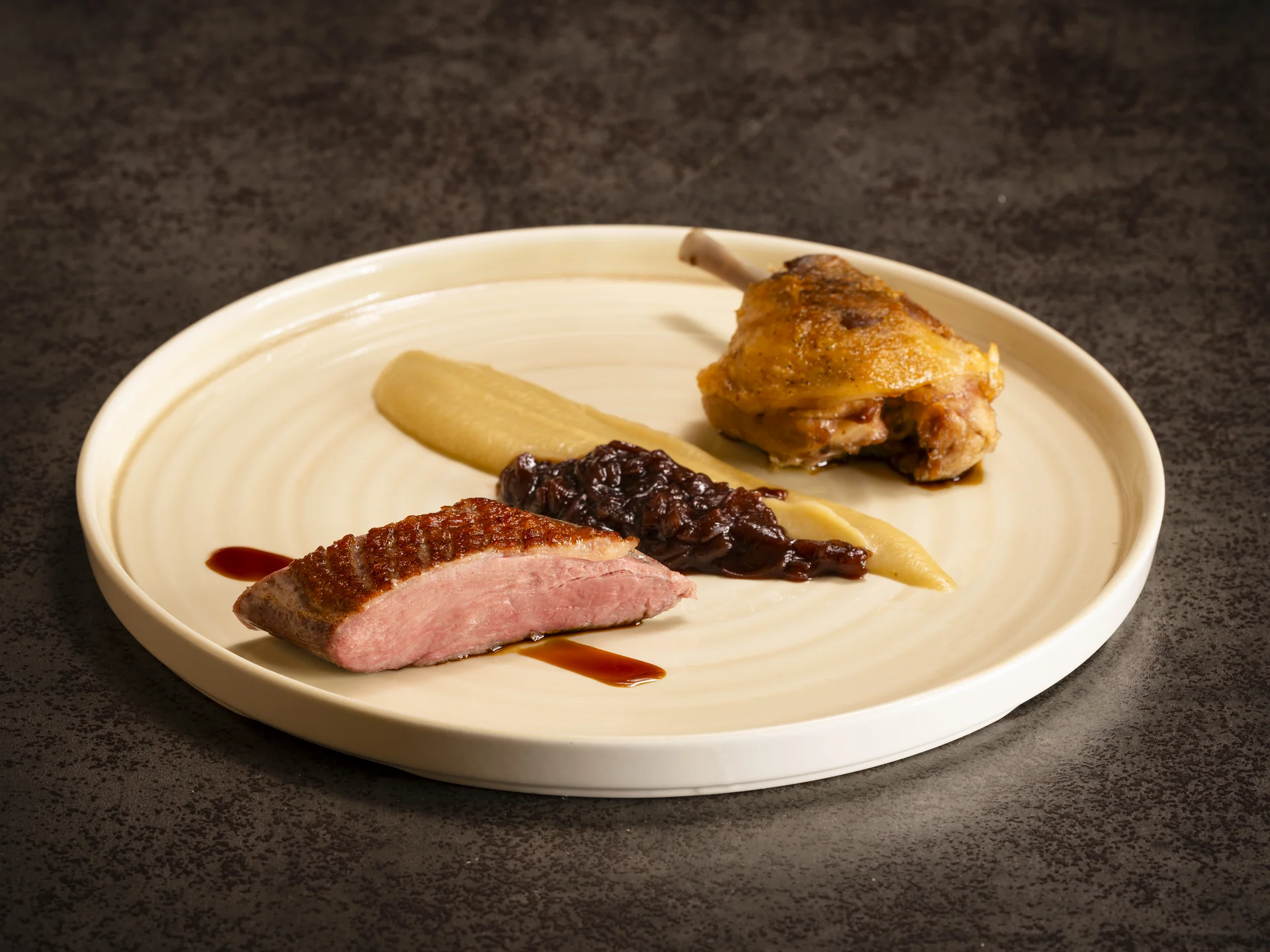 Gourmet-Gericht mit Entenbrust, Entenkeule und Sauce auf cremefarbigem Teller