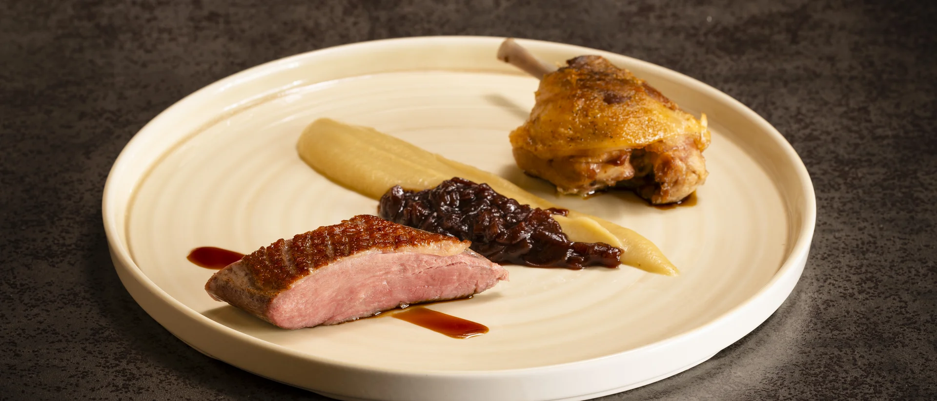 Gourmet-Gericht mit Entenbrust, Entenkeule und Sauce auf cremefarbigem Teller