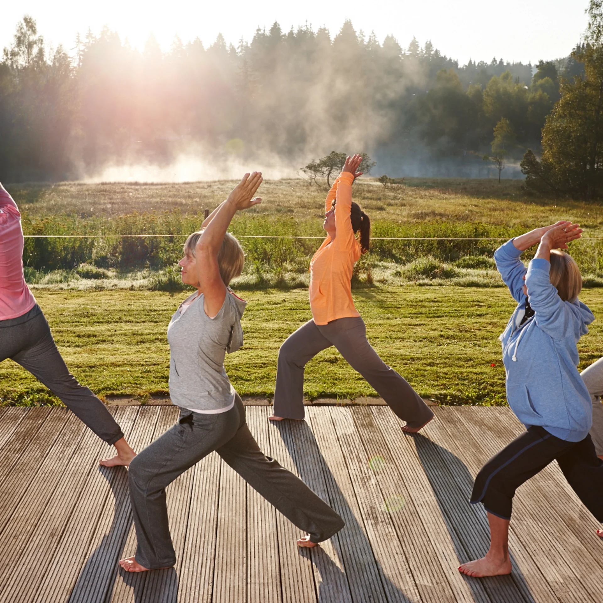 Gruppe übt Yoga im Sonnenlicht auf Holzdeck vor Wald