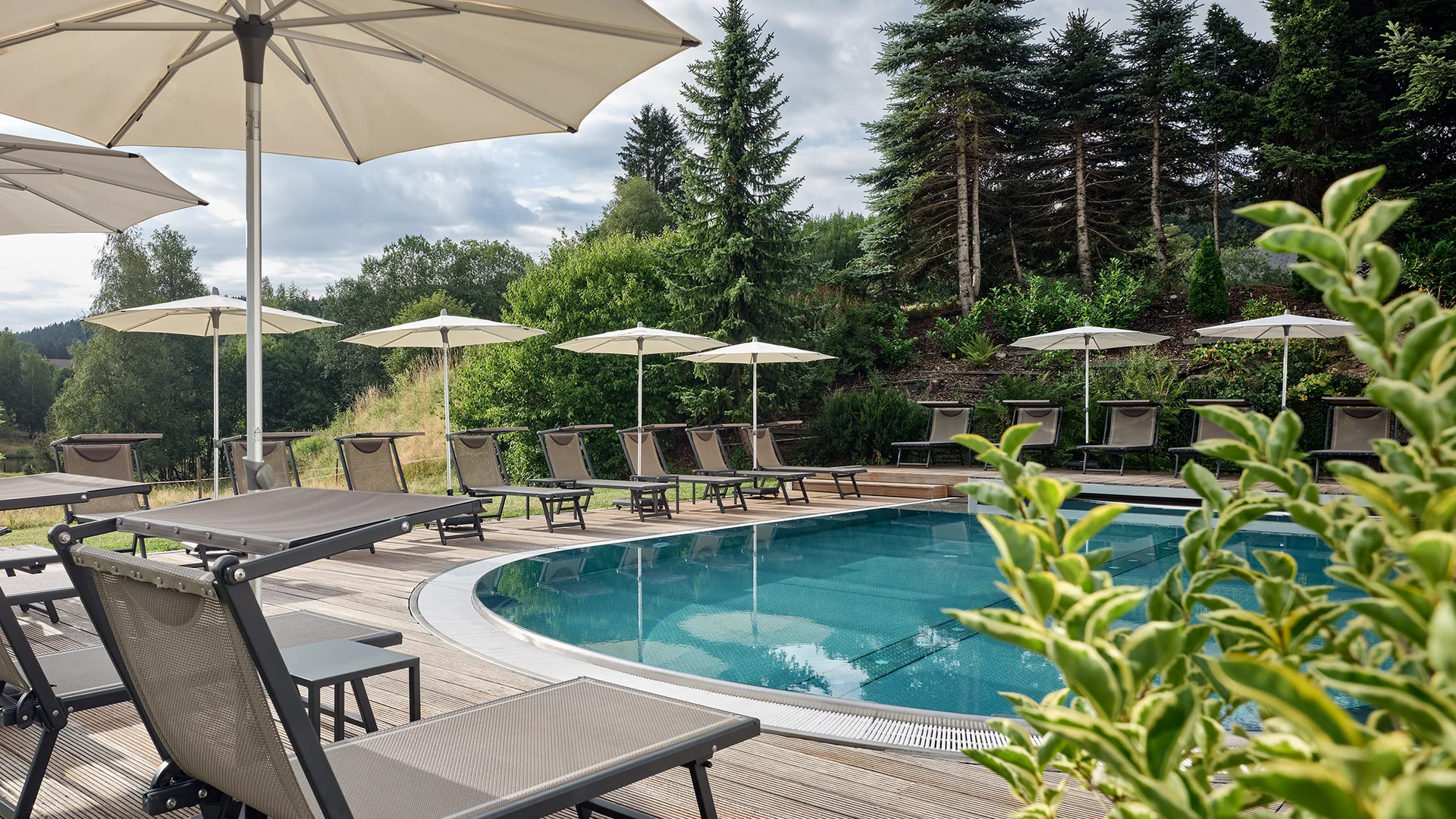 Pool mit Liegestühlen und Sonnenschirmen in einer grünen Landschaft