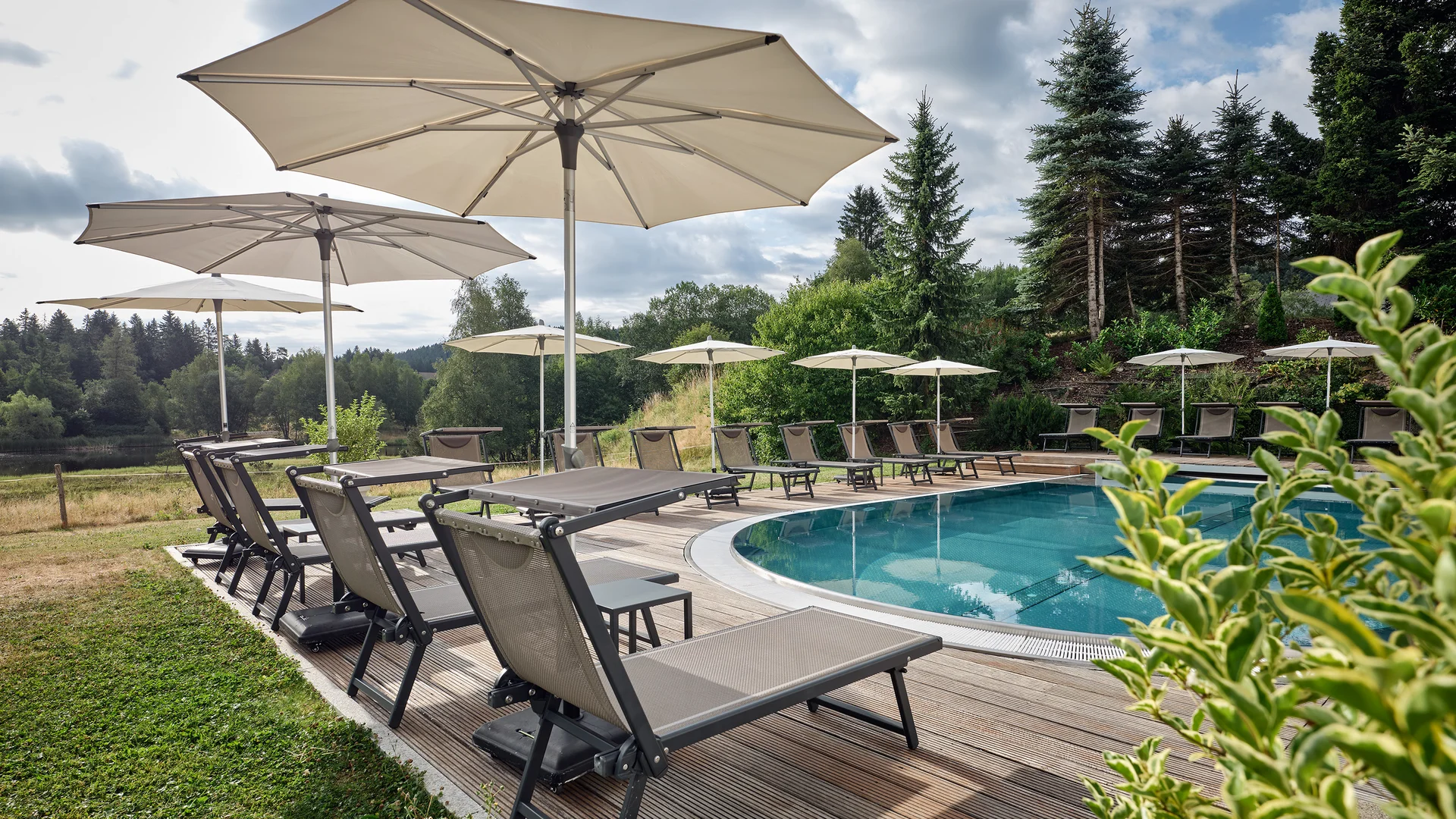 Pool mit Liegestühlen und Sonnenschirmen in einer grünen Landschaft