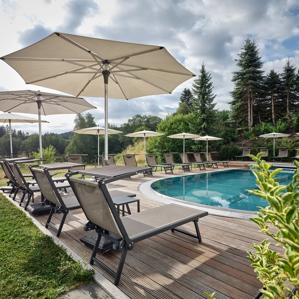Pool mit Liegestühlen und Sonnenschirmen in einer grünen Landschaft