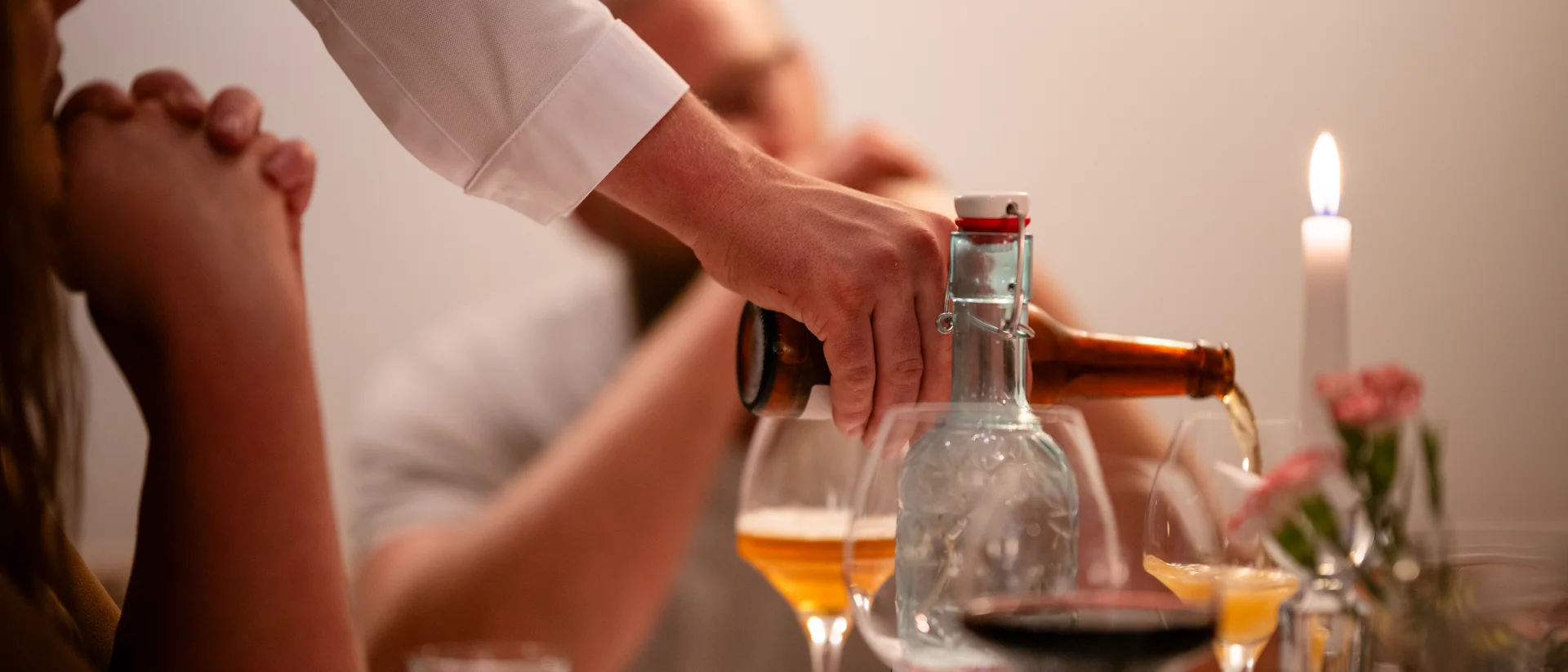 Person gießt Bier in ein Glas bei einem Abendessen mit brennender Kerze