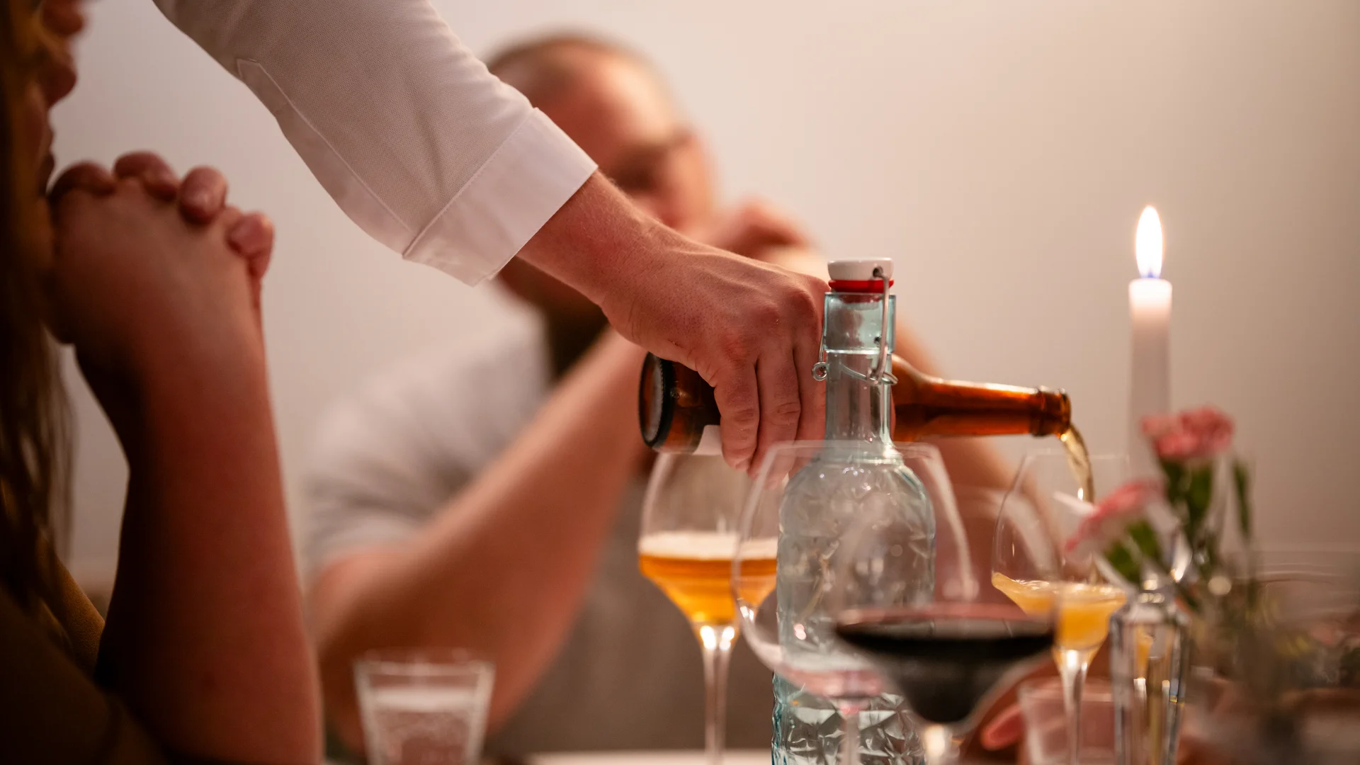 Person gießt Bier in ein Glas bei einem Abendessen mit brennender Kerze