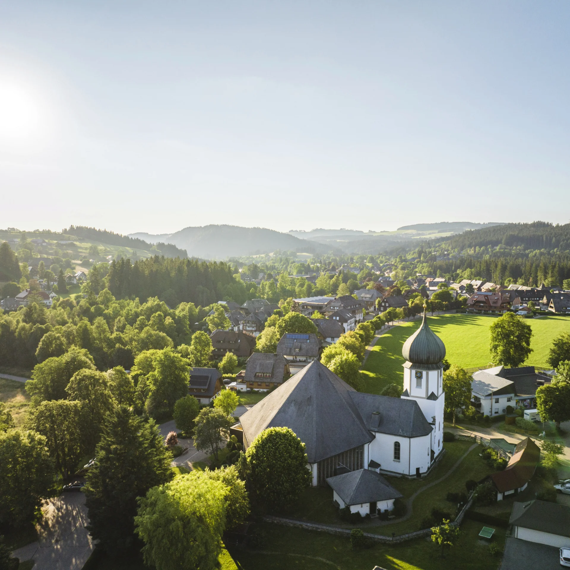 Sonniger Ausblick auf Dorf mit Kirche und grünen Hügeln im Schwarzwald