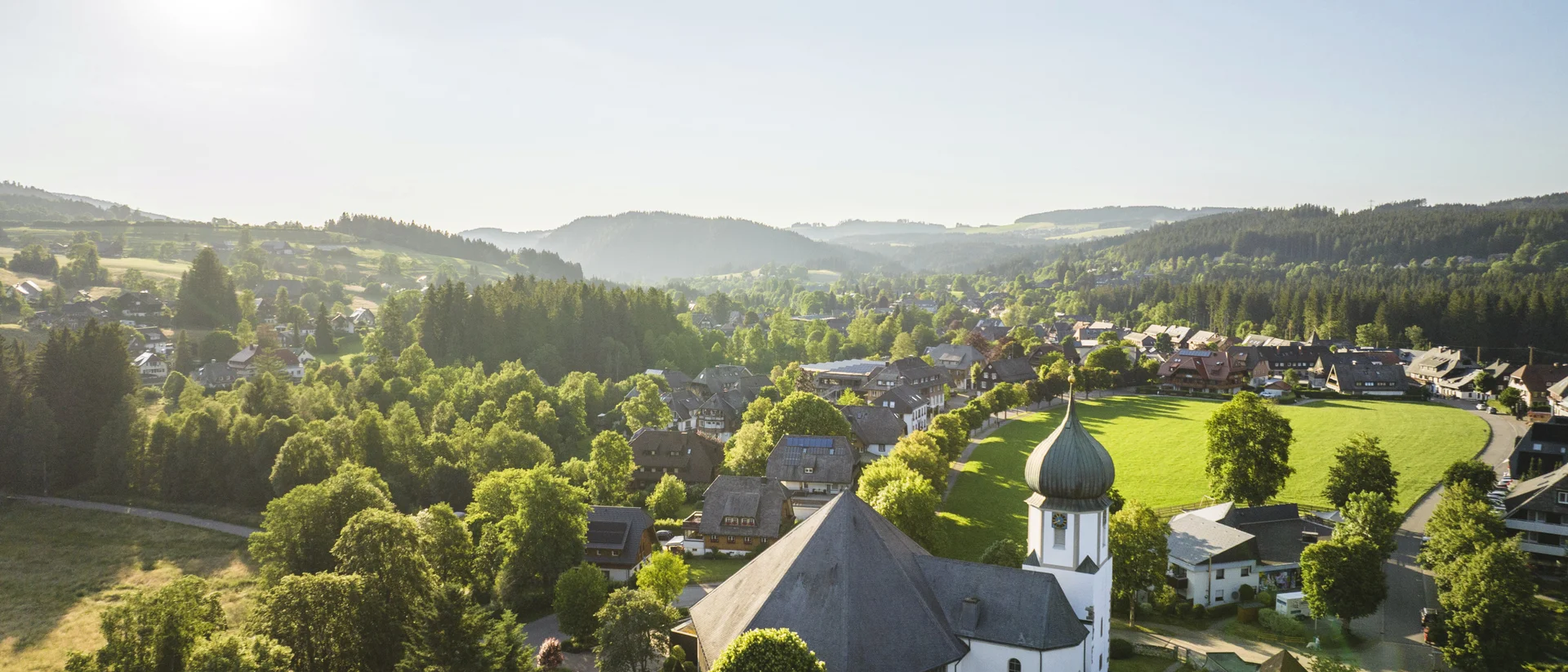 Vue ensoleillée sur village avec église et collines verdoyantes en Forêt-Noire