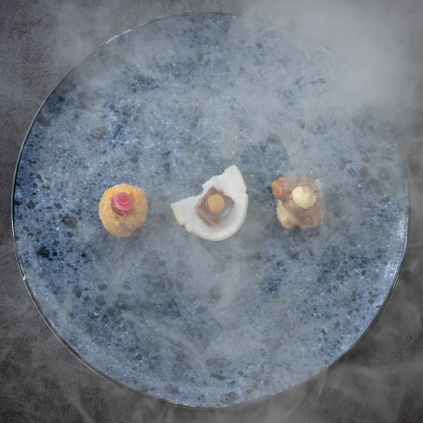 Drei unterschiedliche Appetithäppchen auf blauem Teller mit Nebel