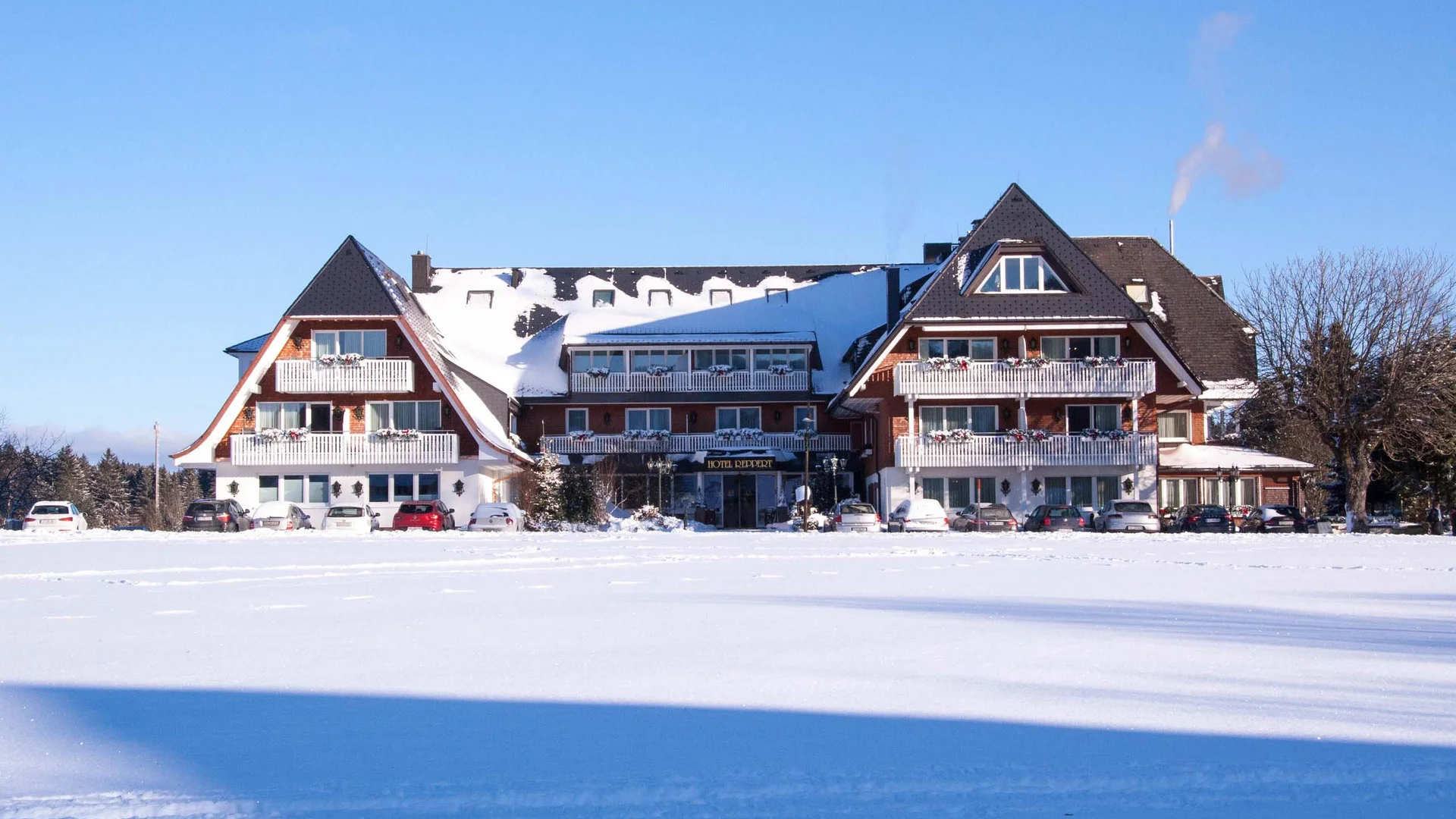 Hotel mit verschneitem Dach vor einer weitläufigen Schneelandschaft