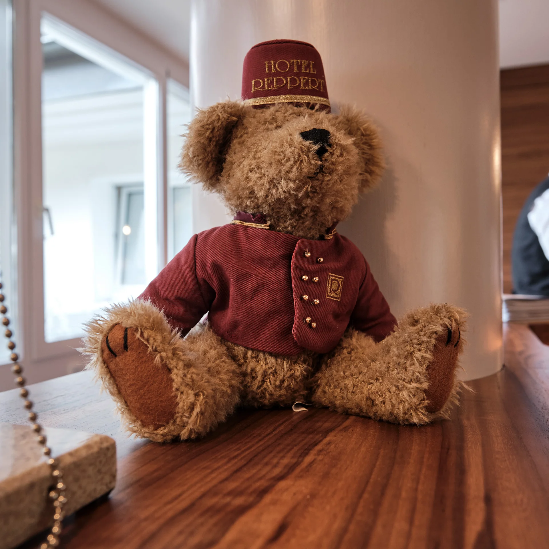 Teddybär mit Hoteluniform und Mütze auf Holztheke im Hotel