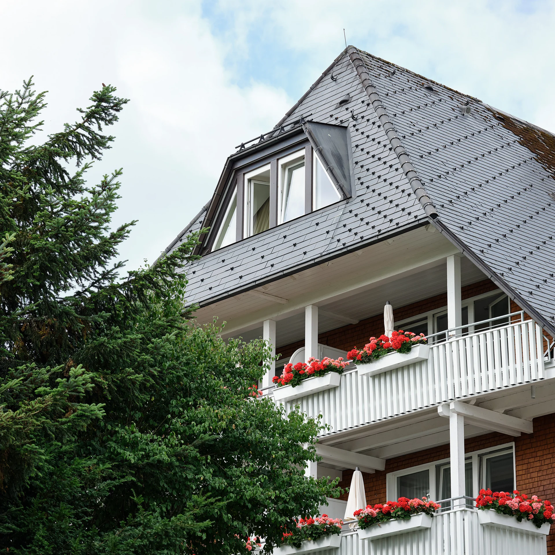 Haus mit schiefergedecktem Dach und blühenden Blumen auf Balkonen