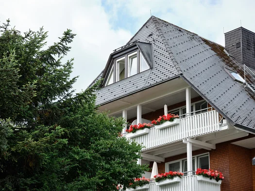 Haus mit schiefergedecktem Dach und blühenden Blumen auf Balkonen